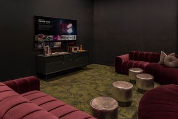 A room with a red couch and ottoman in front of a black wall with a poster on it.